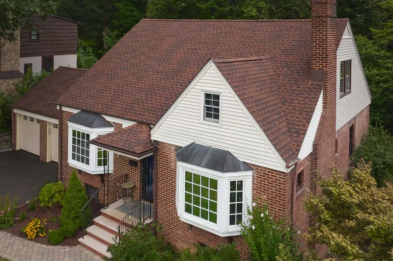 GAF Timberline HDZ shingles in Hickory on a brick and white-siding home with bay windows, from GAF's official Timberline HDZ product page